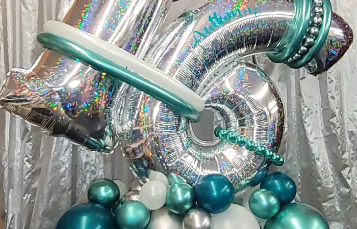 Decorative balloon arrangement with silver, teal, and white balloons on a textured background