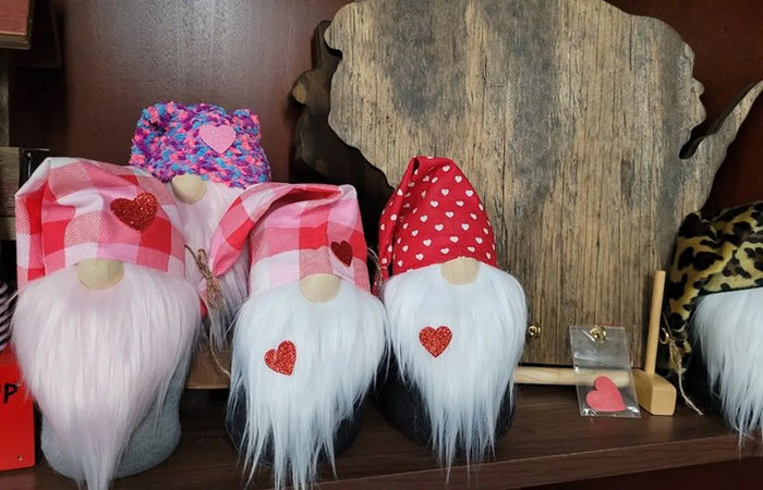 Three gnome figurines with heart details on a wooden shelf.