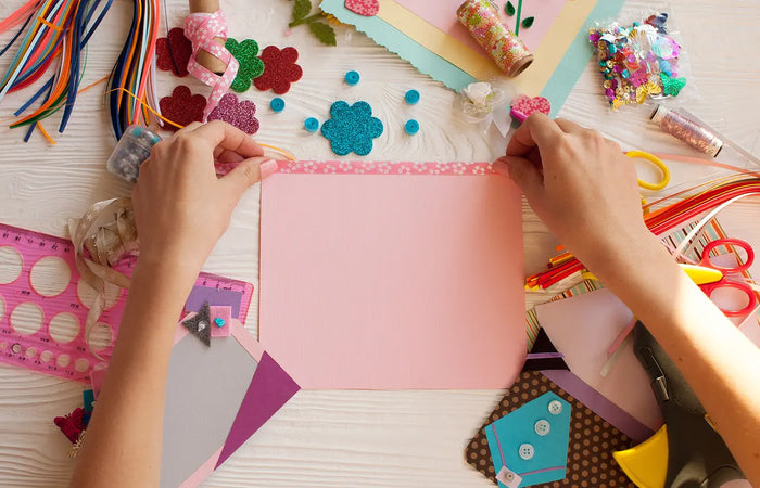 Hands working on a craft project with colorful materials on a table.