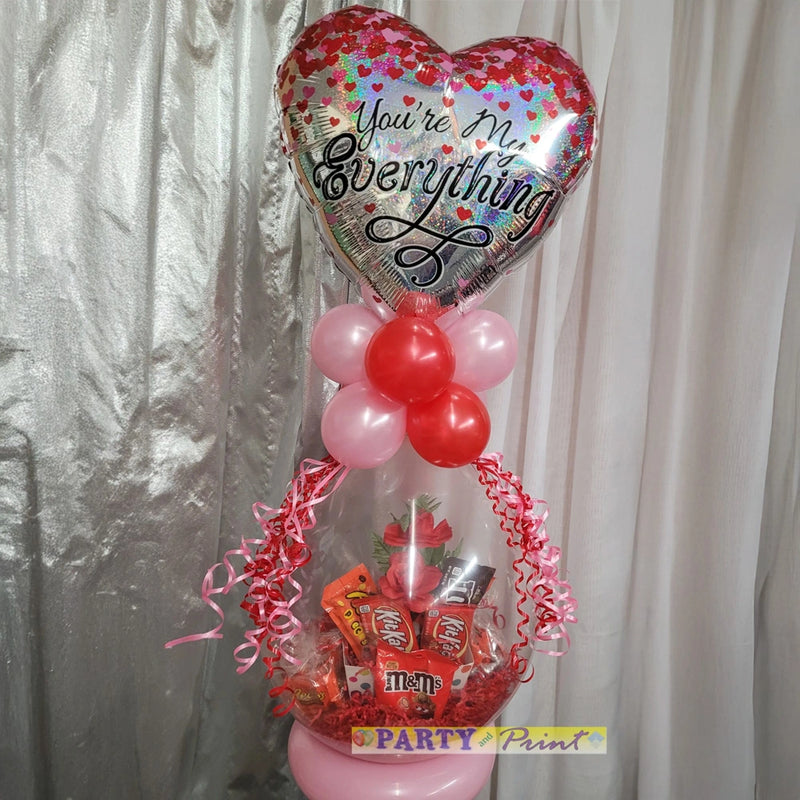 Decorative arrangement with heart-shaped balloon and candy on a stand against a plain background